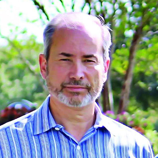 Jack Behar, cofounder of DealerCX, outdoors in a blue striped button-down with a blurred greenery background.