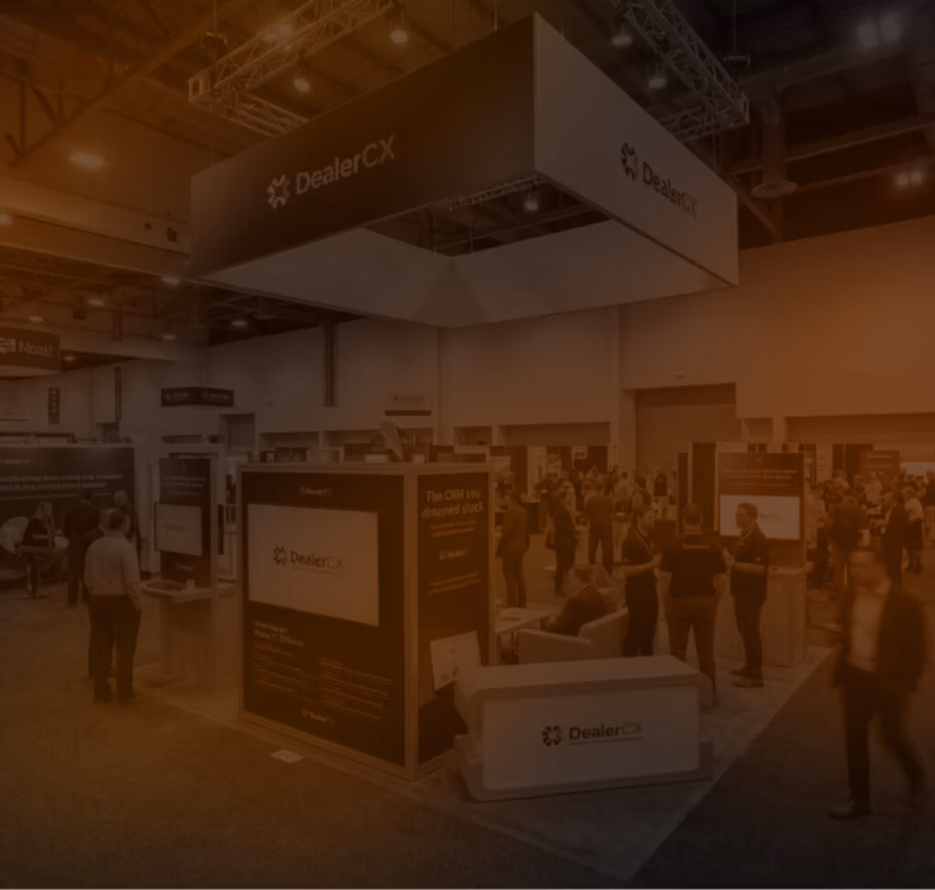 Crowded convention hall featuring the DealerCX booth with large overhead signage, branded display panels, and attendees networking.